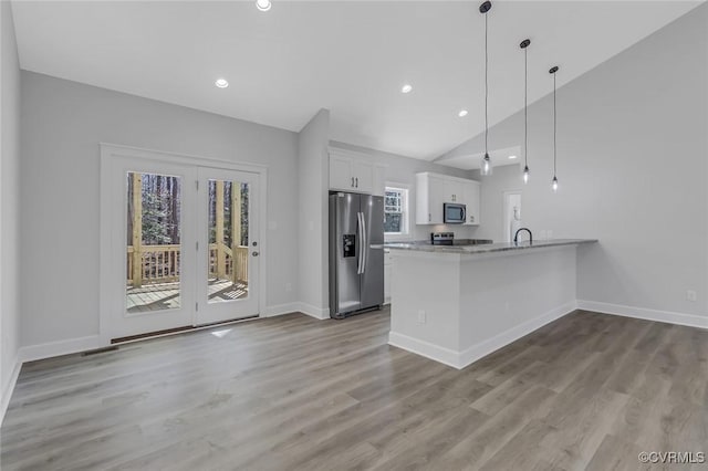 kitchen featuring wood finished floors, stainless steel appliances, a peninsula, white cabinets, and baseboards