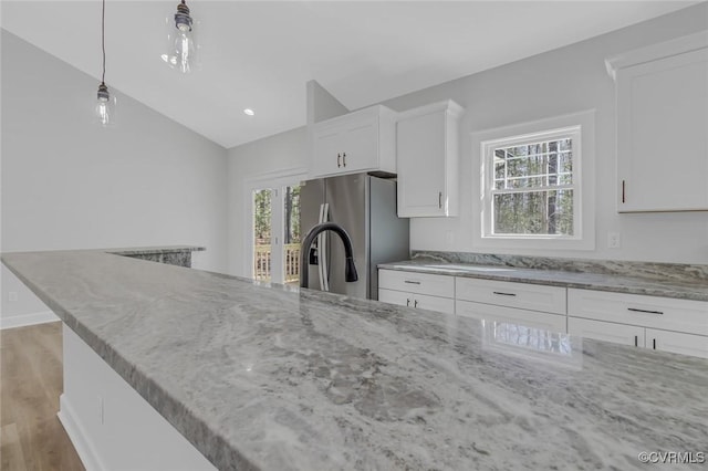 kitchen featuring white cabinetry, light stone counters, stainless steel refrigerator with ice dispenser, and a wealth of natural light