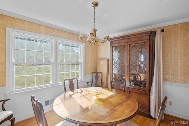 dining area with visible vents, wallpapered walls, light wood-type flooring, ornamental molding, and a notable chandelier