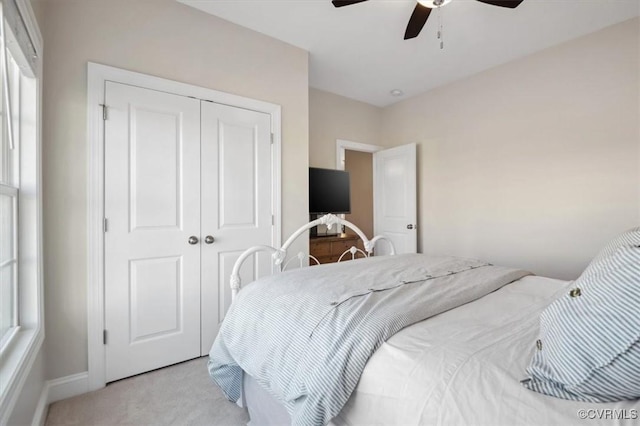 bedroom with a closet, baseboards, light carpet, and a ceiling fan