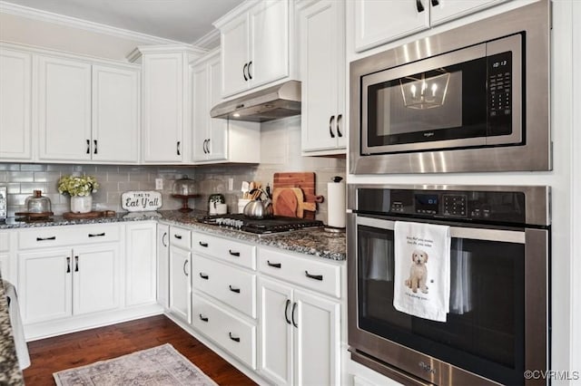 kitchen with under cabinet range hood, white cabinets, appliances with stainless steel finishes, and dark stone counters