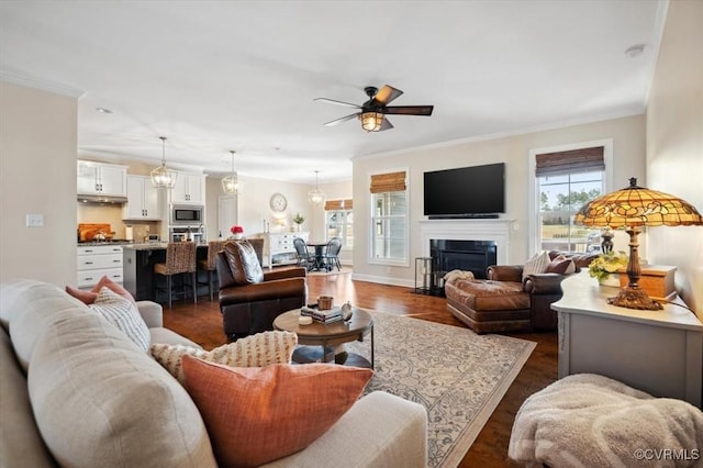 living area with a wealth of natural light, a fireplace with flush hearth, a ceiling fan, and ornamental molding