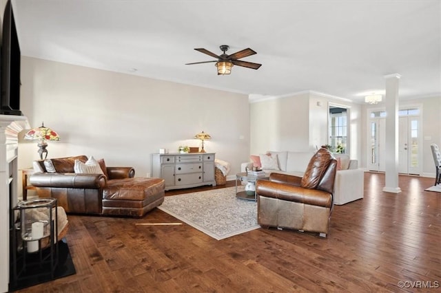 living area featuring a ceiling fan, dark wood finished floors, decorative columns, a fireplace, and crown molding