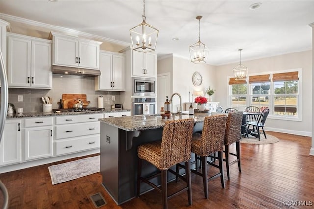 kitchen featuring dark wood-type flooring, under cabinet range hood, appliances with stainless steel finishes, crown molding, and decorative backsplash