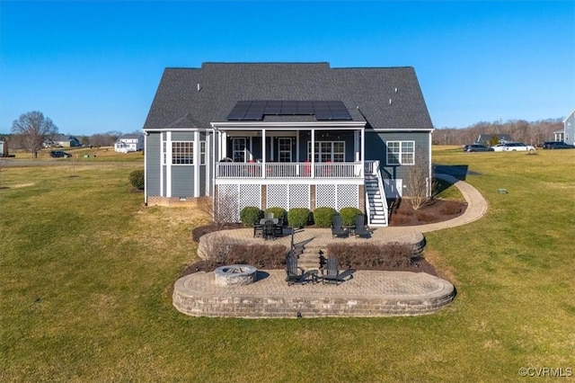 rear view of house with roof mounted solar panels, a lawn, a fire pit, and stairs