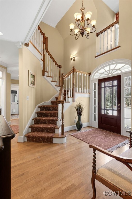 entryway with a notable chandelier, wood finished floors, stairway, baseboards, and a towering ceiling