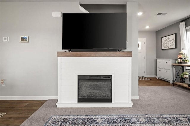 unfurnished living room featuring wood finished floors, visible vents, baseboards, and a glass covered fireplace