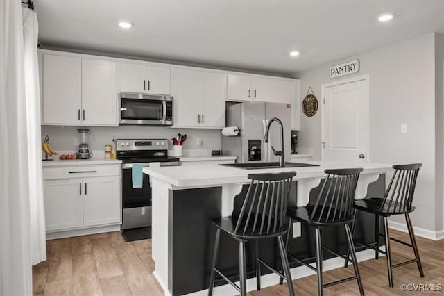 kitchen featuring white cabinetry, a kitchen island with sink, light wood finished floors, and stainless steel appliances