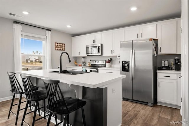 kitchen with wood finished floors, visible vents, an island with sink, a sink, and appliances with stainless steel finishes