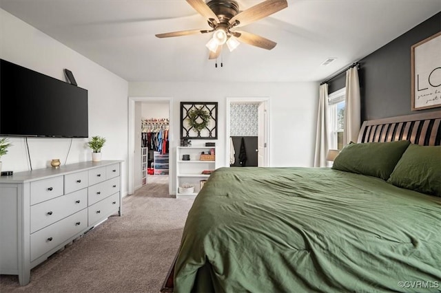 bedroom with a spacious closet, light colored carpet, and a ceiling fan