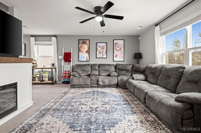 carpeted living room featuring visible vents, a ceiling fan, and a glass covered fireplace