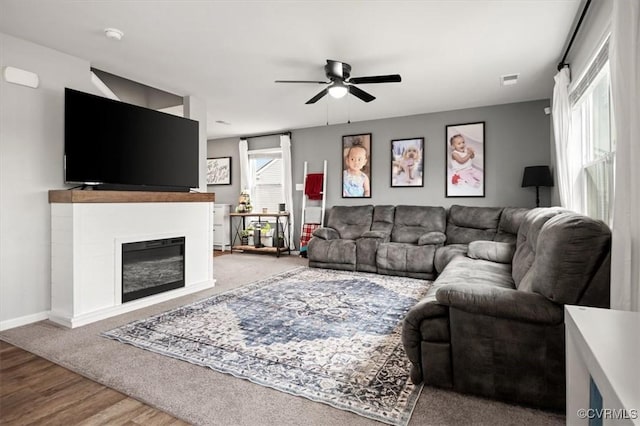 living area with ceiling fan, baseboards, wood finished floors, and a glass covered fireplace