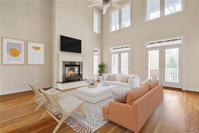 living area featuring a glass covered fireplace, baseboards, wood finished floors, and a ceiling fan