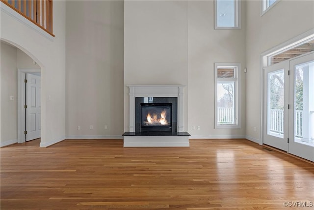 unfurnished living room with baseboards, a high ceiling, wood finished floors, and a high end fireplace