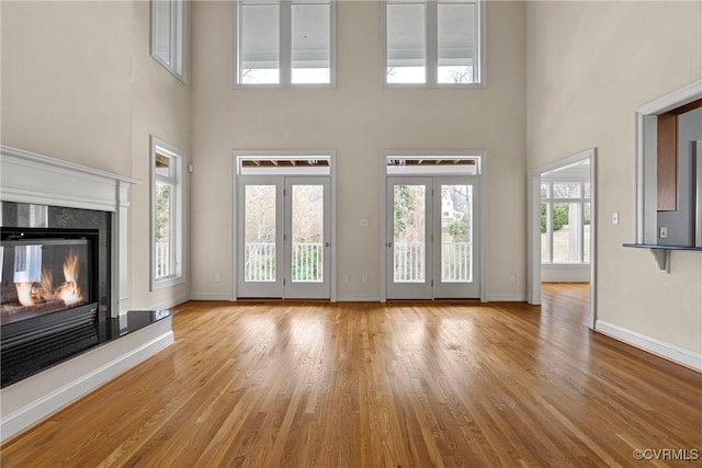 unfurnished living room with a premium fireplace, a high ceiling, baseboards, and wood finished floors