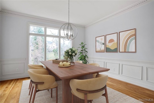 dining space with crown molding, a decorative wall, wainscoting, light wood-style flooring, and a notable chandelier