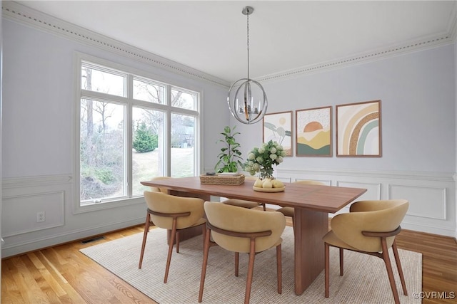 dining space with visible vents, an inviting chandelier, light wood-style flooring, crown molding, and a decorative wall