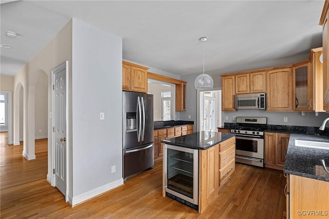 kitchen featuring wood finished floors, beverage cooler, arched walkways, a sink, and stainless steel appliances