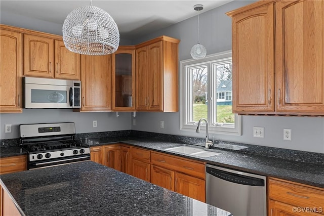 kitchen featuring pendant lighting, a sink, dark stone counters, appliances with stainless steel finishes, and glass insert cabinets