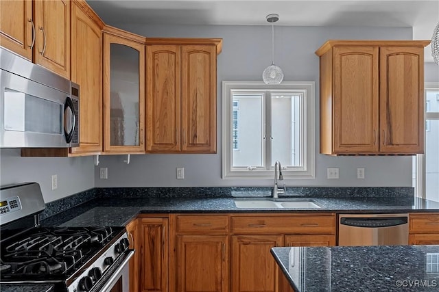 kitchen with dark stone countertops, a sink, stainless steel appliances, glass insert cabinets, and decorative light fixtures