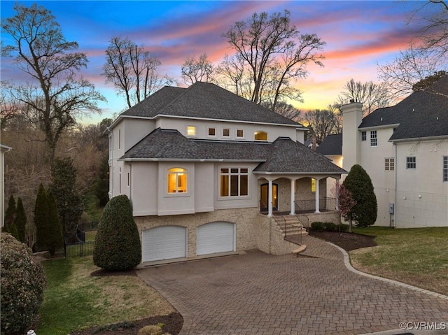 view of front of home with a porch, stucco siding, a lawn, decorative driveway, and an attached garage