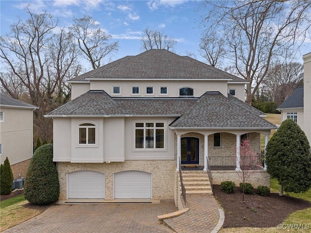 view of front of house featuring roof with shingles, an attached garage, covered porch, stucco siding, and decorative driveway