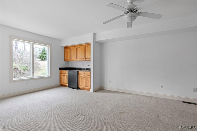 kitchen featuring baseboards, a sink, black dishwasher, light carpet, and dark countertops