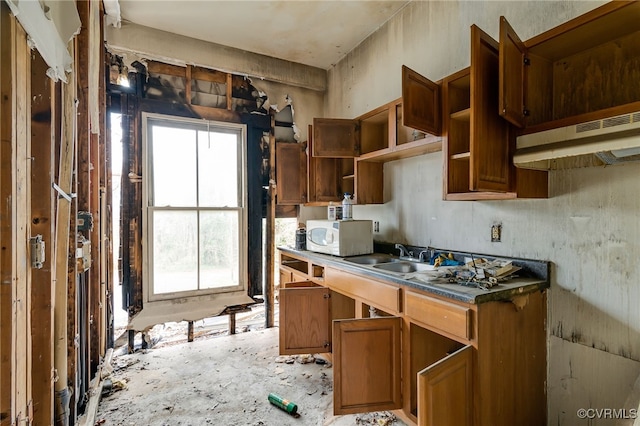 kitchen featuring white microwave, open shelves, under cabinet range hood, brown cabinetry, and a sink