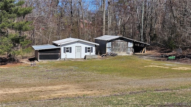 view of front of house featuring an outbuilding, a wooded view, a front lawn, and a carport