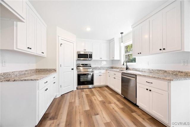 kitchen featuring decorative light fixtures, light wood-type flooring, light stone counters, appliances with stainless steel finishes, and white cabinetry