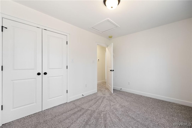 unfurnished bedroom featuring a closet, carpet flooring, attic access, and baseboards