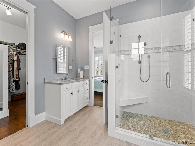 full bath featuring vanity, a shower stall, a spacious closet, and wood finished floors