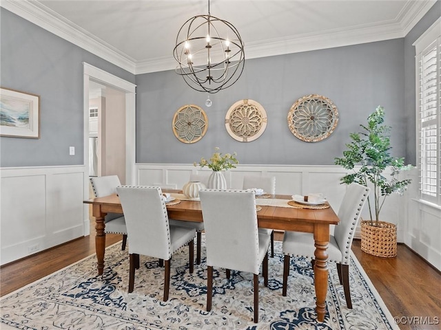 dining space featuring ornamental molding, wainscoting, an inviting chandelier, wood finished floors, and a decorative wall