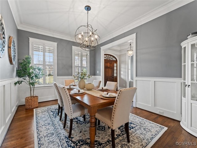 dining area with dark wood-type flooring, ornamental molding, a wainscoted wall, and a chandelier