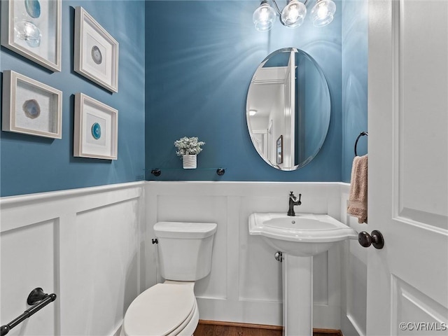 half bath featuring a decorative wall, toilet, and a wainscoted wall