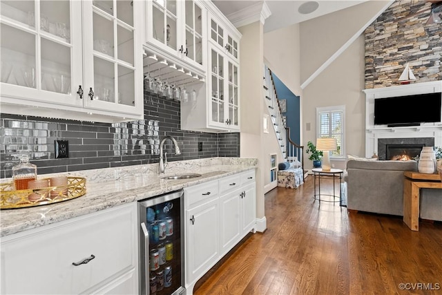 kitchen with beverage cooler, a sink, backsplash, a lit fireplace, and dark wood-style flooring