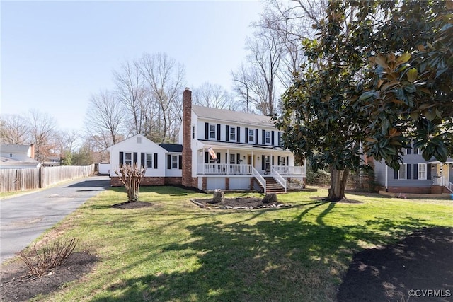 view of front of home with a front yard, fence, a porch, a chimney, and aphalt driveway