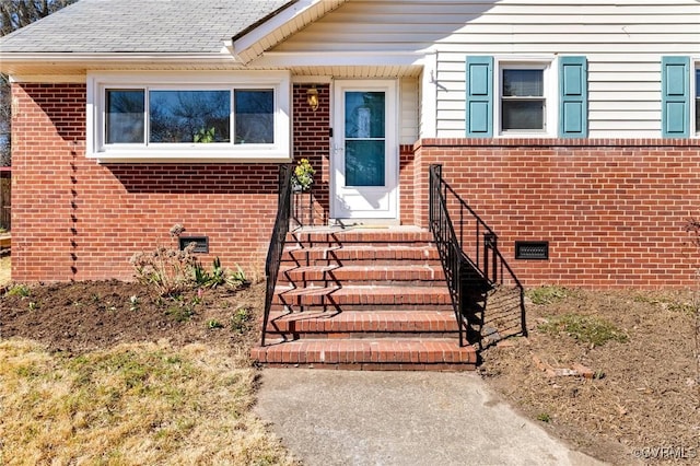 entrance to property with crawl space, a shingled roof, and brick siding