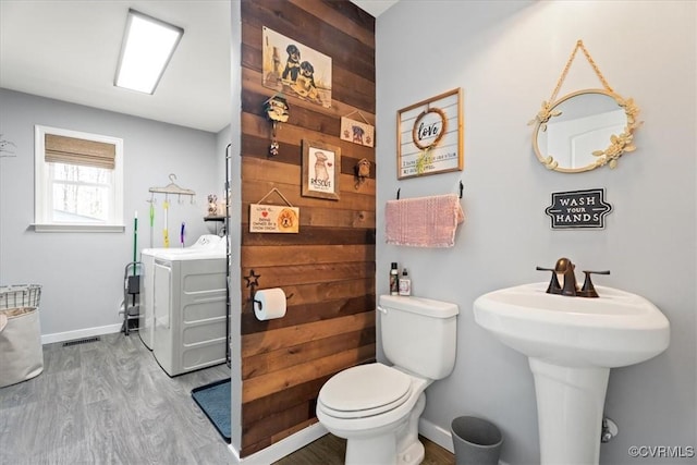 bathroom featuring toilet, washer / clothes dryer, wood finished floors, wood walls, and baseboards