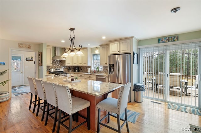 kitchen featuring a center island, a breakfast bar area, decorative backsplash, appliances with stainless steel finishes, and wall chimney exhaust hood