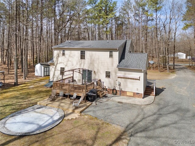 back of house featuring a shingled roof, aphalt driveway, a patio area, a deck, and crawl space