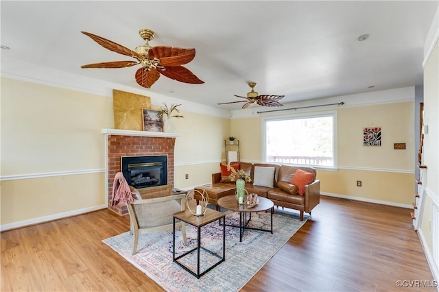 living room featuring baseboards, a ceiling fan, wood finished floors, and a fireplace