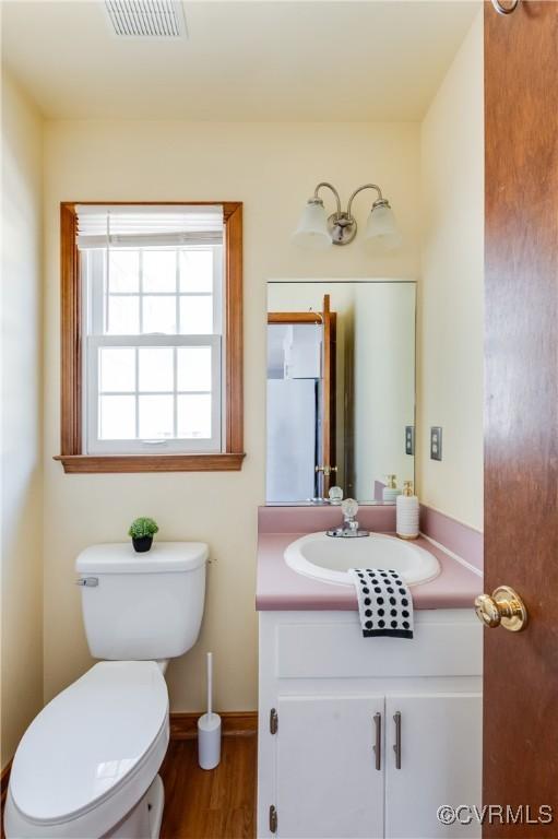 half bath featuring visible vents, baseboards, toilet, wood finished floors, and vanity