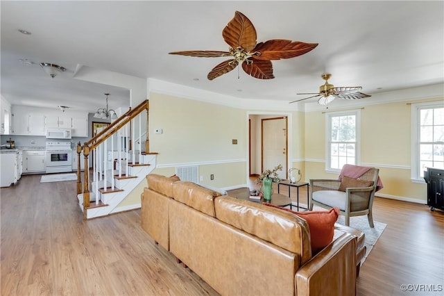 living area featuring a ceiling fan, visible vents, light wood finished floors, baseboards, and stairs