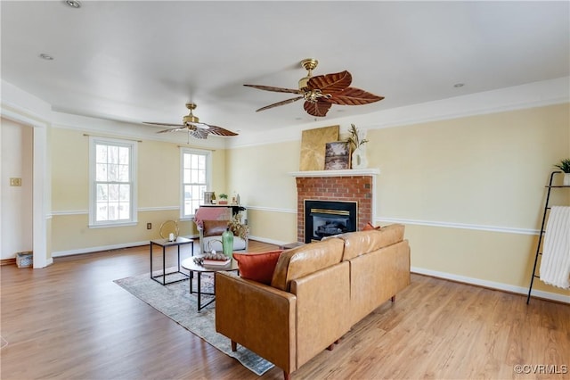 living room featuring baseboards, light wood-style floors, a fireplace, and a ceiling fan