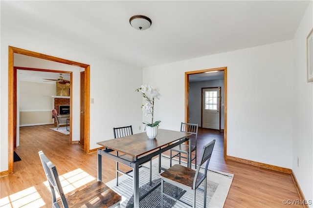 dining area with ceiling fan, light wood-type flooring, baseboards, and a fireplace with raised hearth