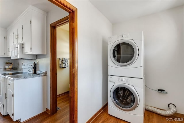 laundry area featuring baseboards, wood finished floors, laundry area, and stacked washing maching and dryer