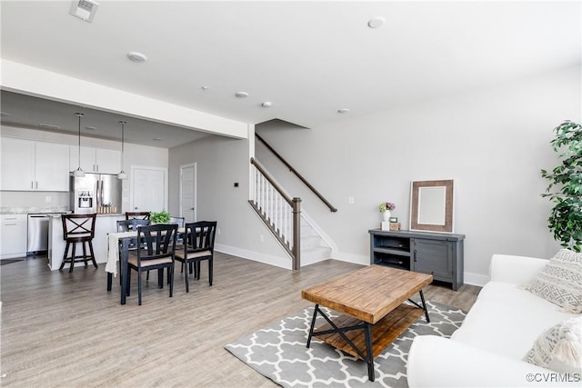 living room featuring stairs, baseboards, visible vents, and light wood finished floors