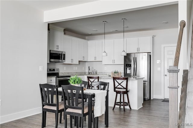 kitchen with pendant lighting, a kitchen breakfast bar, dark wood-type flooring, and appliances with stainless steel finishes