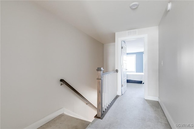 hallway with an upstairs landing, carpet flooring, baseboards, and visible vents